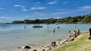 Una playa con agua cristalina, barcos y gente.