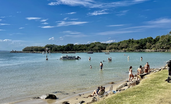 Una playa con agua cristalina, barcos y gente.