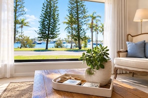 Una habitación con vista a un puerto deportivo, una mesa de madera con una bandeja, una planta en maceta y un sofá con cojines.