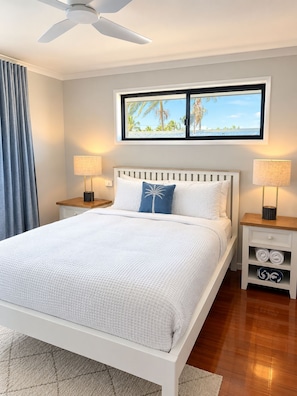 Un dormitorio con cama, mesitas de noche, ventilador de techo y ventana con vistas, además de una mesita con toallas.