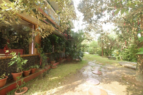 A garden pathway leading to a building with a balcony, surrounded by potted plants and a stone wall. - Birders Den Eco Resort (Nainital)