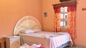 Une chambre avec deux lits, un téléviseur fixé au mur et une fenêtre ornée de rideaux à motifs.