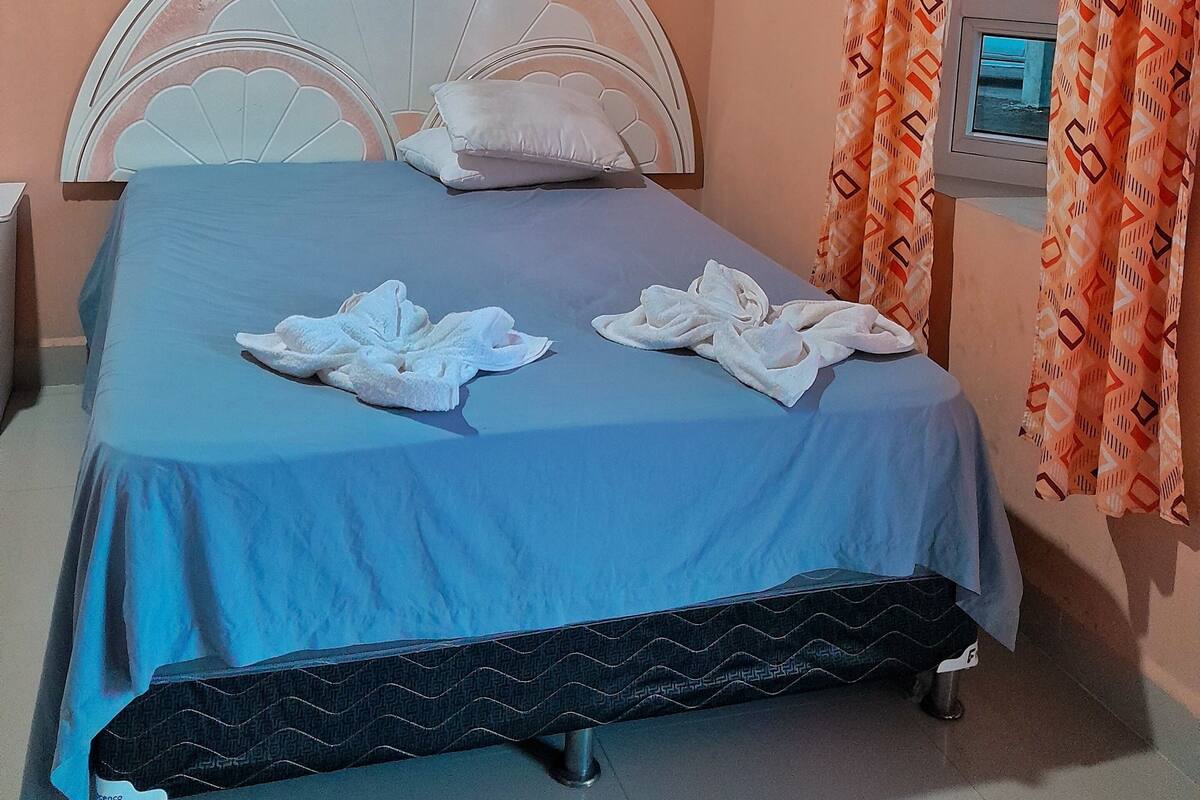 A bedroom with a bed, pillows, a TV, and patterned curtains.