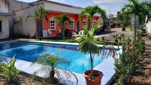 Une piscine entourée de plantes en pot et un bâtiment à la façade rouge.