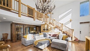 A spacious living room with a large sectional sofa, wooden flooring, and a staircase with a wooden railing. - Spacious, Luxury, Picturesque "Mountain High Manor"- Ski Resort Town! (Wrightwood)