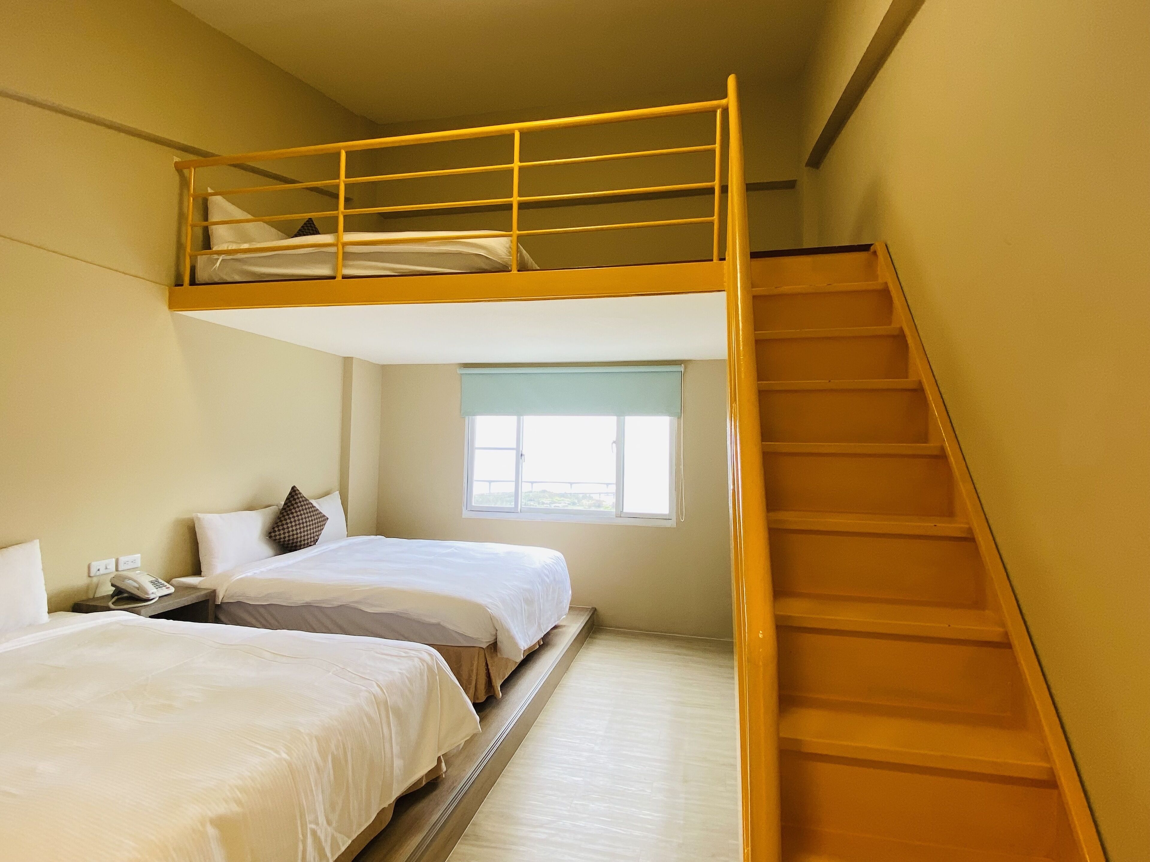 A dormitory room with bunk beds, a small window, a telephone, and a wooden staircase.