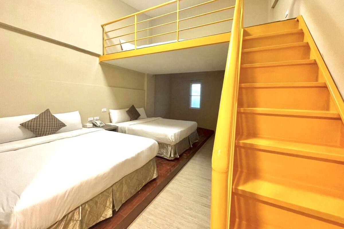 Ein Hotelzimmer mit Etagenbett, einem Einzelbett und einer Treppe.