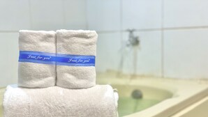 Zwei ordentlich gefaltete Handtücher mit einer blauen Schleife liegen in einer Badewanne in einem Badezimmer, in dem eine Dusche zu sehen ist.
