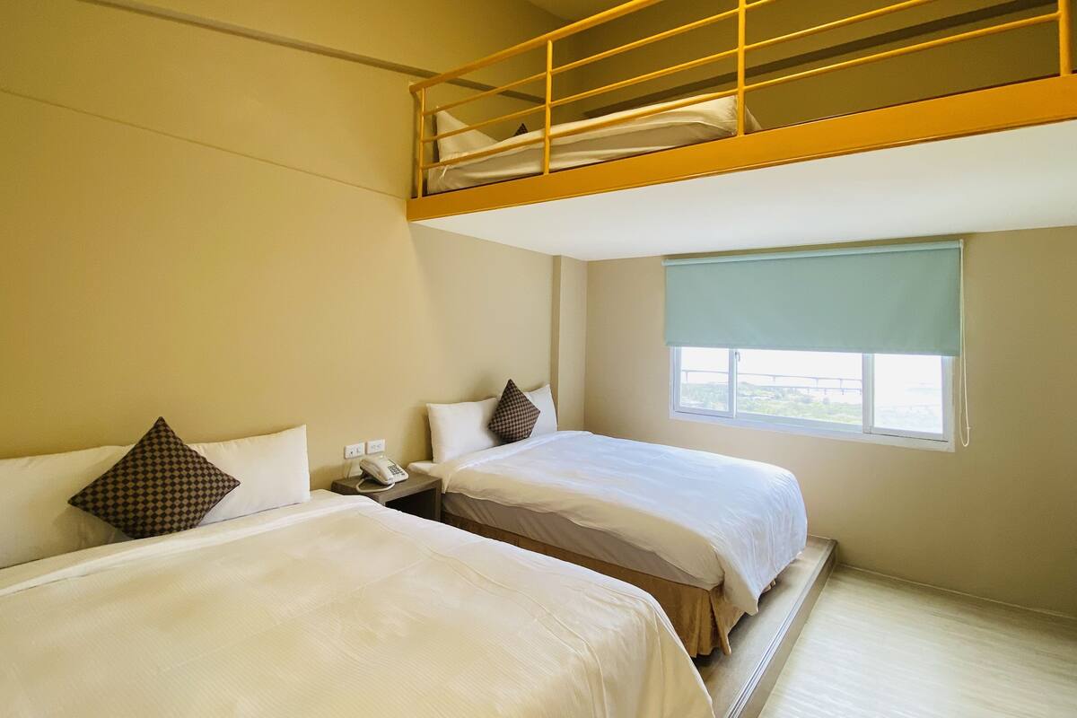 Ein Hotelzimmer mit zwei Betten, darunter ein Etagenbett und ein Nachttischtelefon, sowie ein Fenster mit Blick.