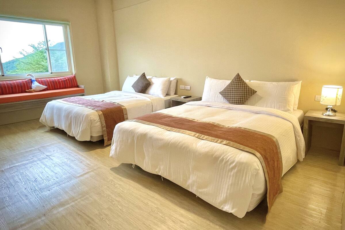 Ein Hotelzimmer mit zwei Betten, einer Fensterbank mit rotem Kissen und einer Lampe auf dem Nachttisch.