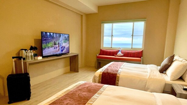 Ein Hotelzimmer mit zwei Betten, einem Fernseher auf einem Schrank, einem Fenster mit Blick und einer Bank mit Schwan-Verzierung.
