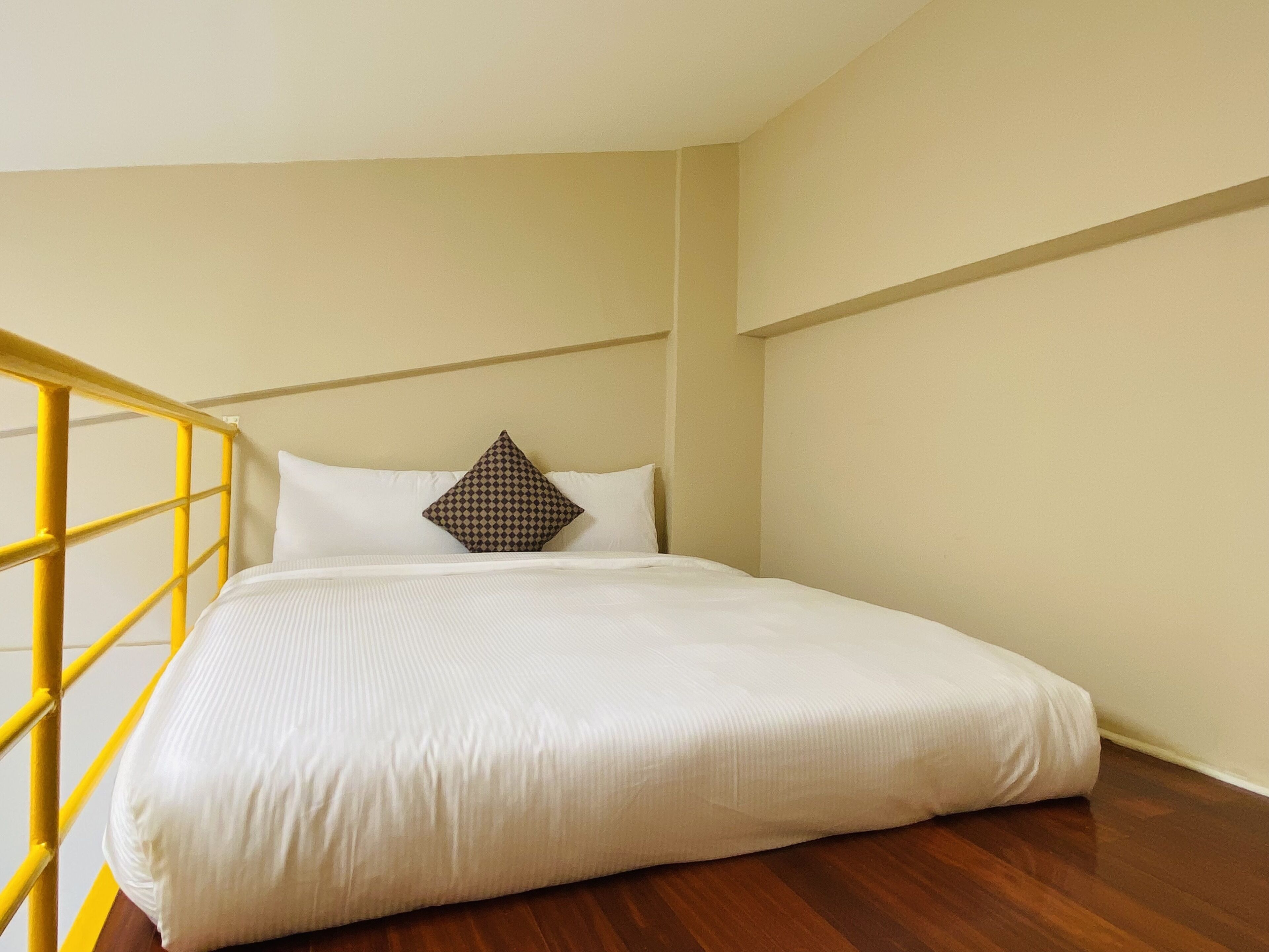 Una cama individual con ropa de cama blanca, un cojín estampado y una barandilla amarilla.