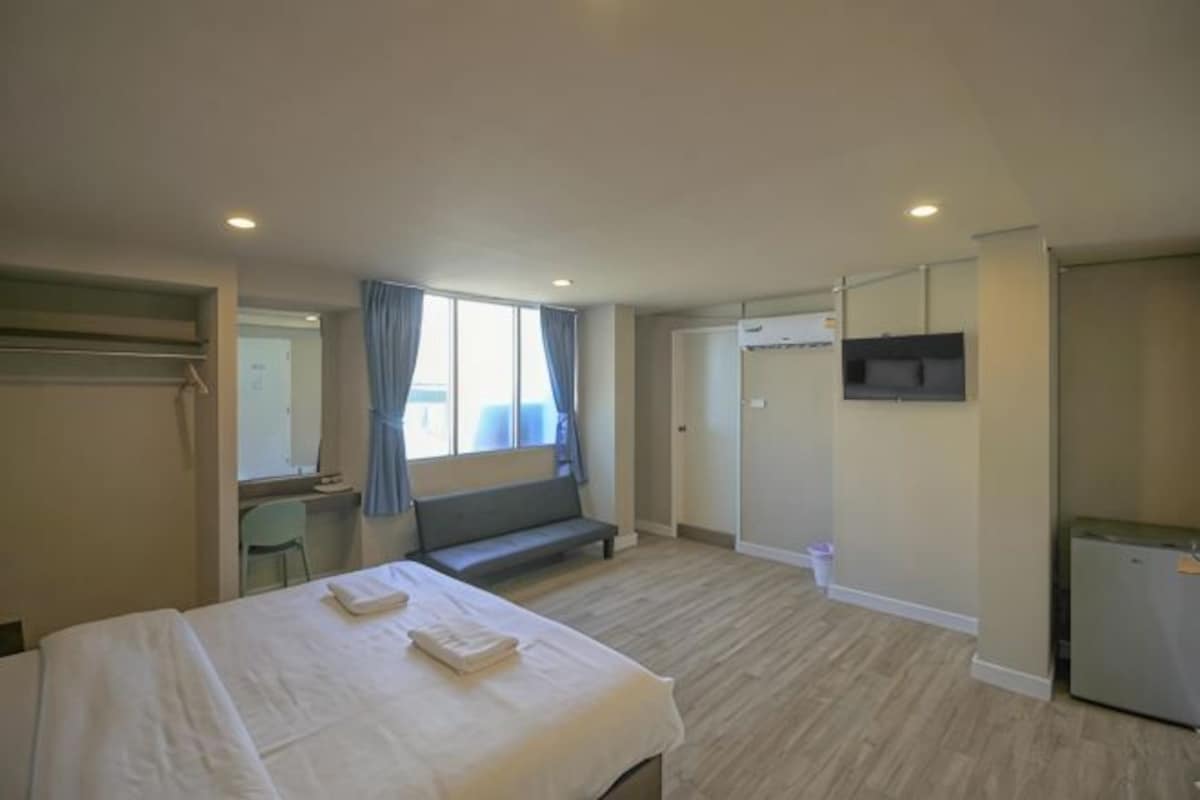 A hotel room with a bed, a desk, a bench, a TV, and a door.