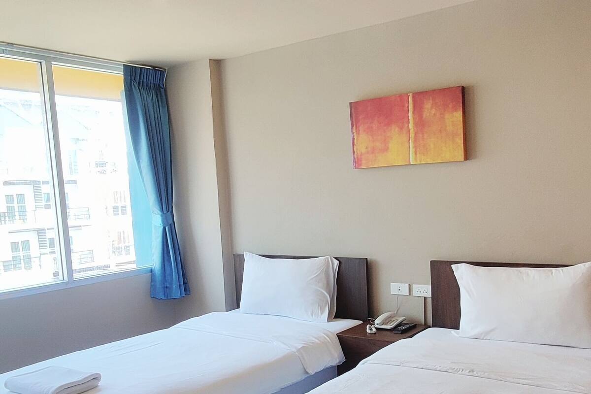 A hotel room with two beds, a window with curtains, a painting on the wall, and a nightstand with a phone.