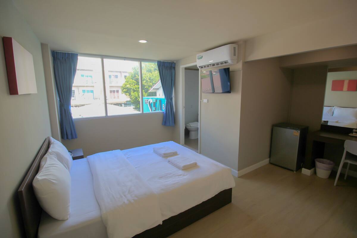 A hotel room with a bed, a desk, an air conditioner, and a view of the outside.