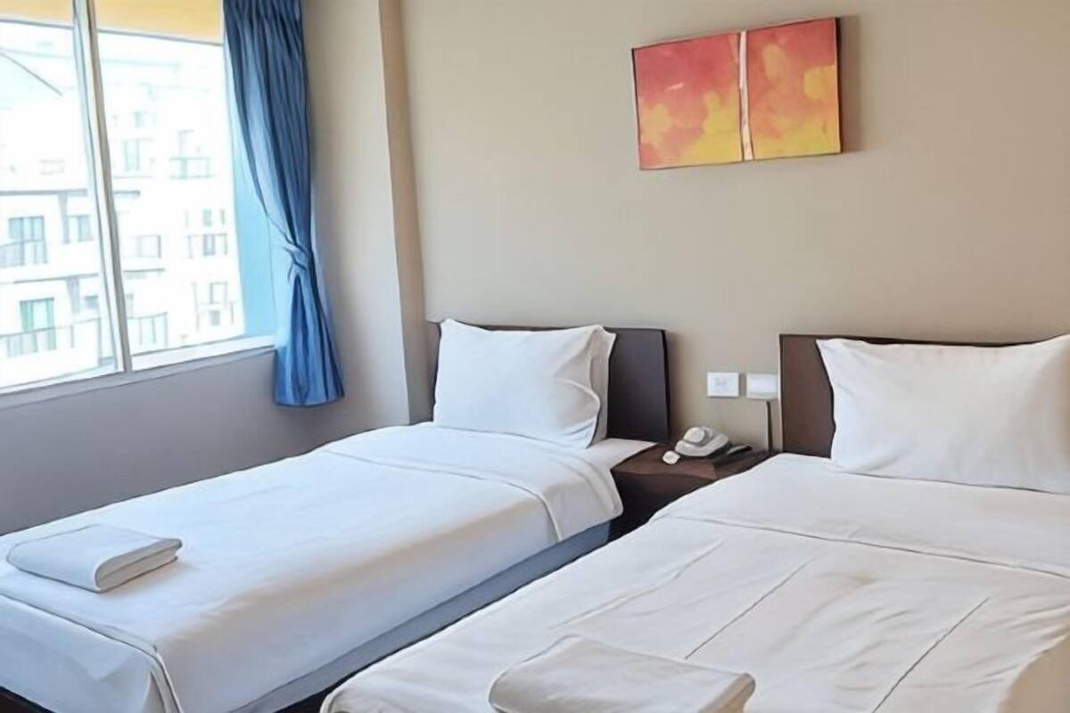 Two beds with white linens, a nightstand with a phone, and a window with blue curtains.