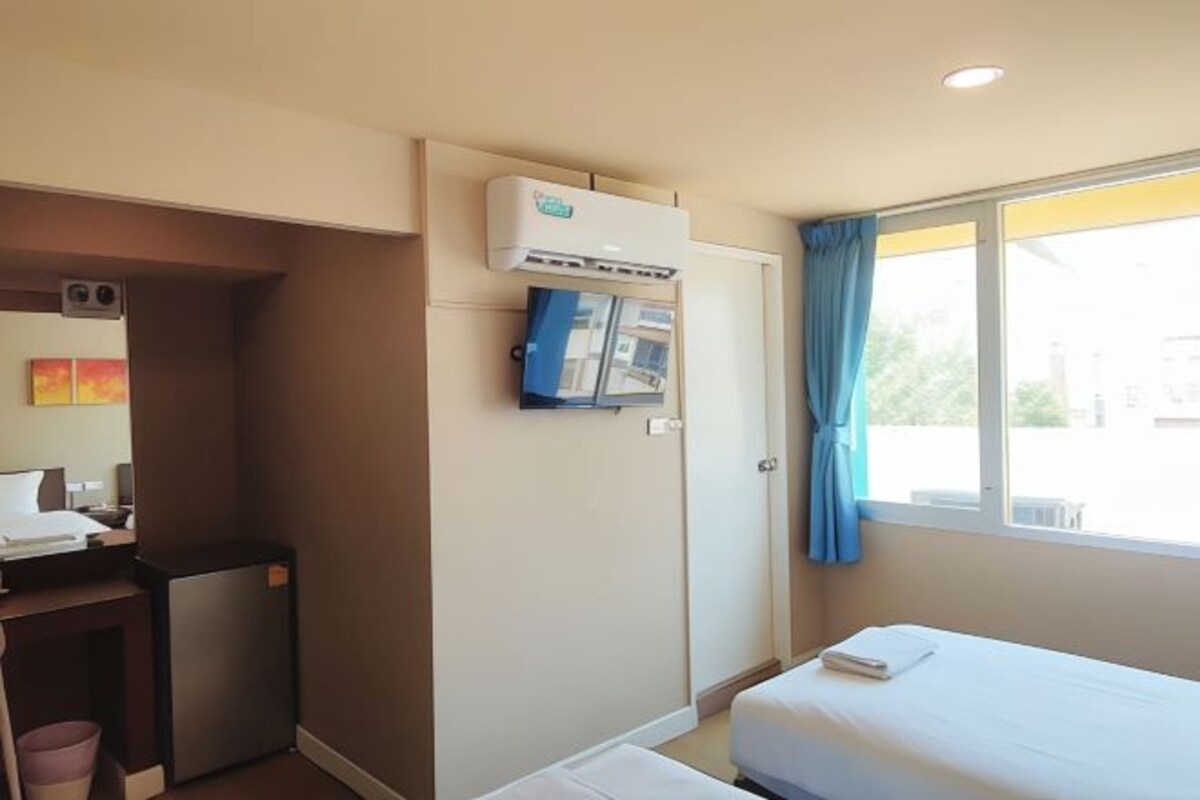 Habitación de hotel con cama, escritorio, refrigerador pequeño, aire acondicionado y ventana con cortinas.