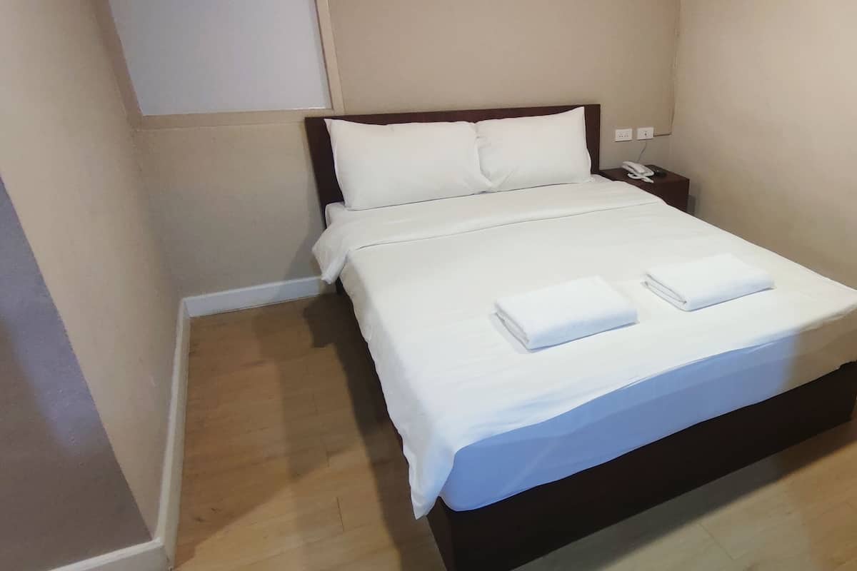 A neatly made bed with white linens and two folded towels, a bedside phone, and a small nightstand.