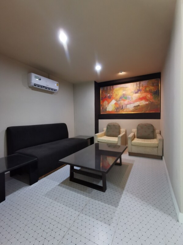 Una sala de estar moderna con un sofá negro, dos sillones, una mesa de centro de vidrio y un cuadro abstracto grande en la pared.