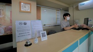 A hotel reception desk with a clock, a whiteboard, and a sign indicating no smoking.