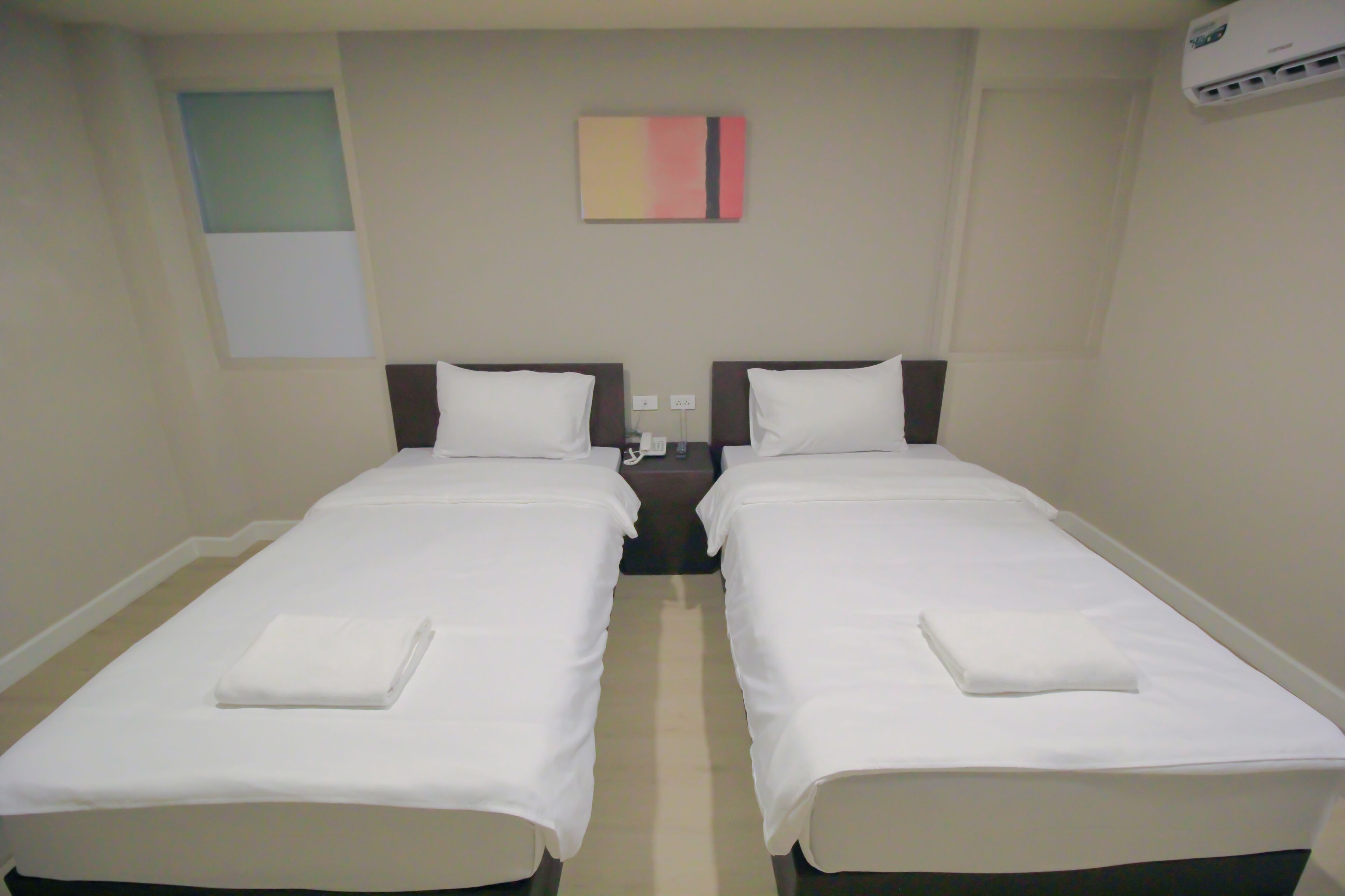 A twin room with two single beds, a bedside table, a wall-mounted air conditioner, and a small painting.