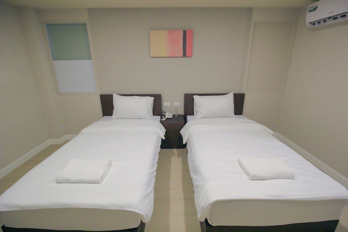 Une chambre double avec deux lits simples, une table de chevet, un climatiseur mural et un petit tableau.