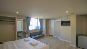 A hotel room with a bed, a bench, a desk, a chair, a TV, and a door.