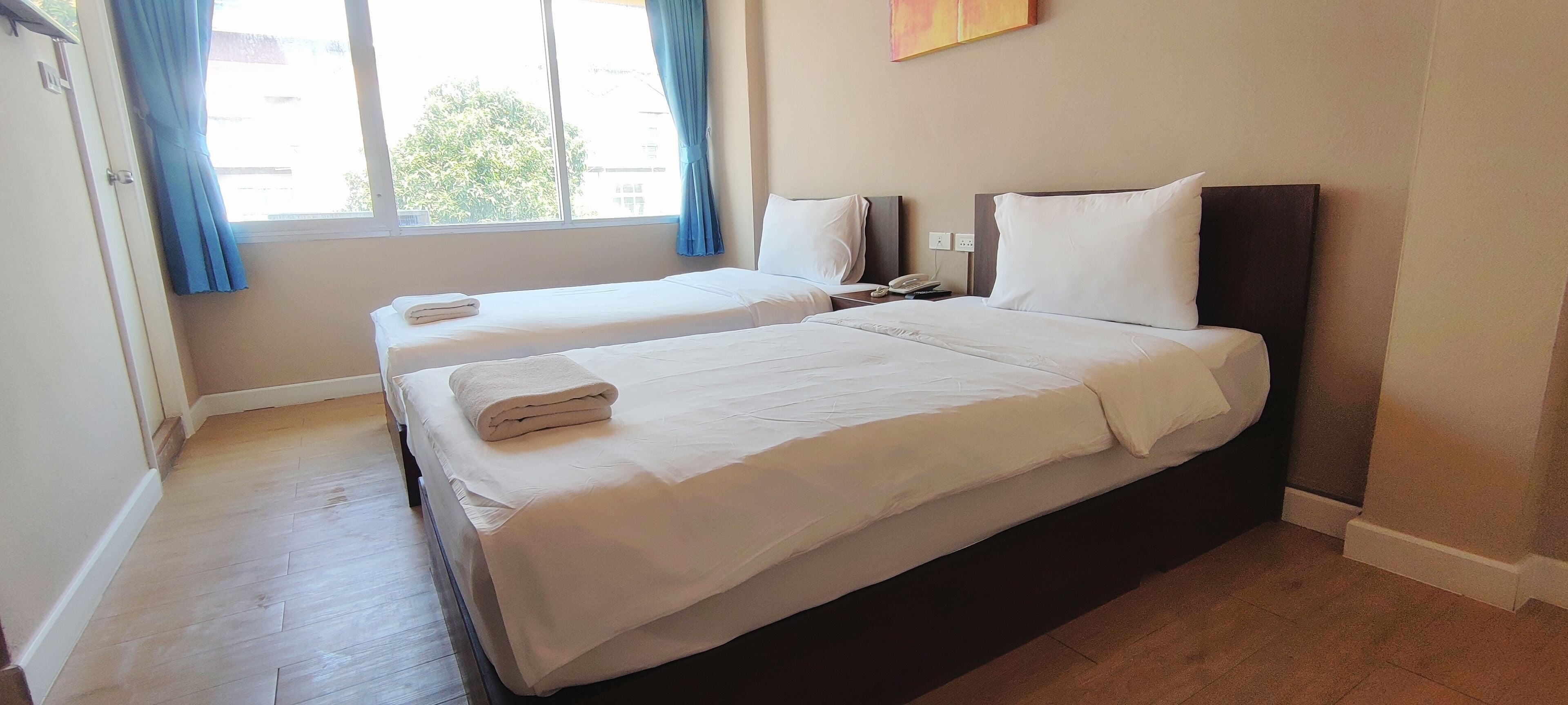 Une chambre d’hôtel avec deux lits, une fenêtre avec des rideaux, une table de chevet avec un téléphone et un interrupteur fixé au mur.