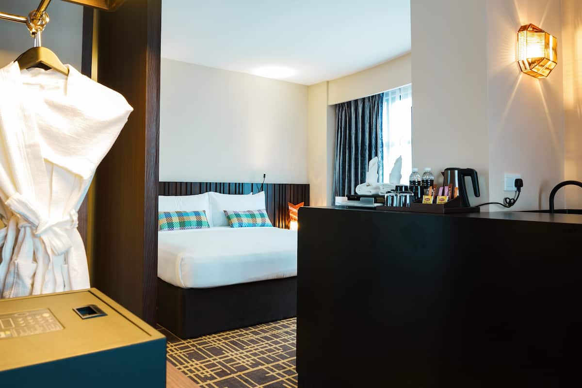 A hotel room with a bed, a desk, a robe hanging, and a mirror.