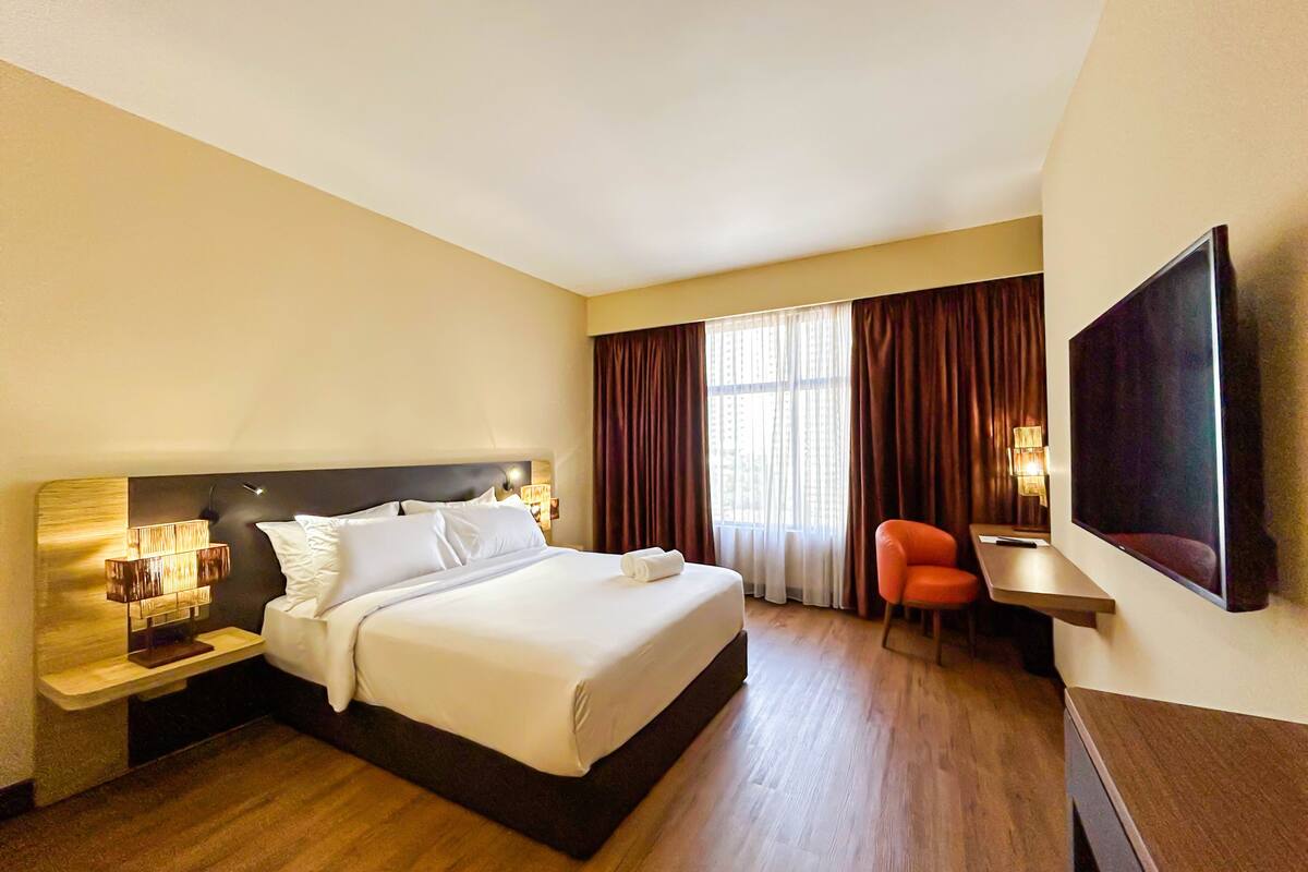 A hotel room with a bed, a desk, a chair, a TV, and a window with curtains.