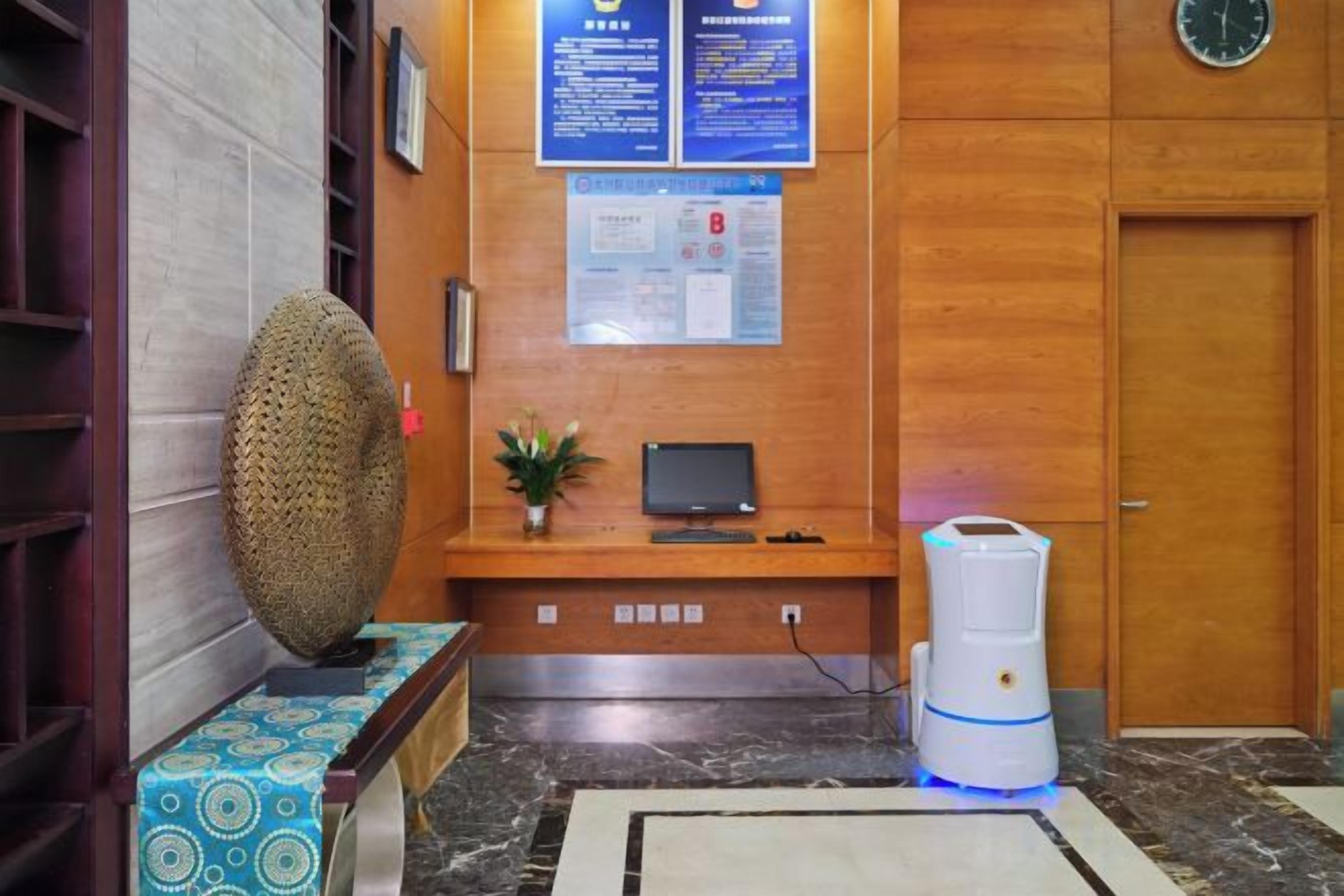 A reception area with a wooden reception desk, a monitor, a plant, and a water dispenser.