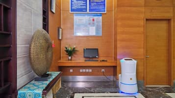 A reception area with a wooden reception desk, a monitor, a plant, and a water dispenser.