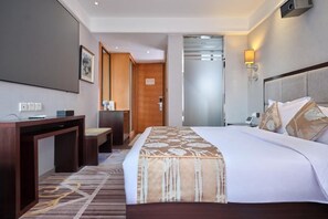 Een hotelkamer met een bed, bureau, stoel en een deur die naar een andere kamer leidt.