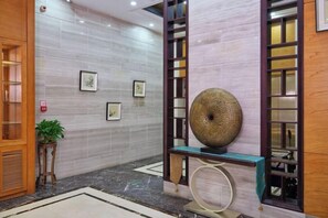 Un hall d’entrée avec un sol en marbre, des œuvres d’art encadrées accrochées au mur, un comptoir d’accueil en bois et un grand vase décoratif.