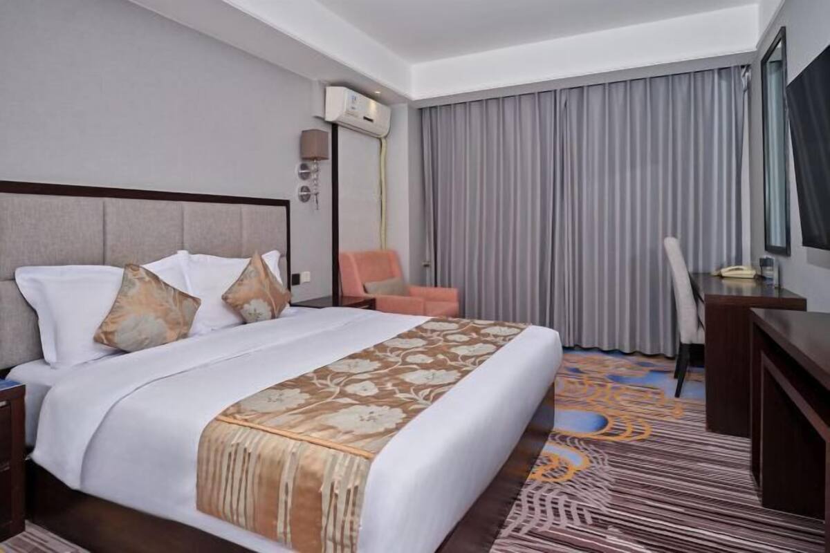 Een hotelkamer met een bed, een bureau, een stoel, een televisie en een raam met gordijnen.