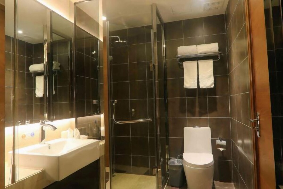 Ein modernes Badezimmer mit einer Glaskabine zur Dusche, einem Waschbecken mit Spiegel und einer Toilette.