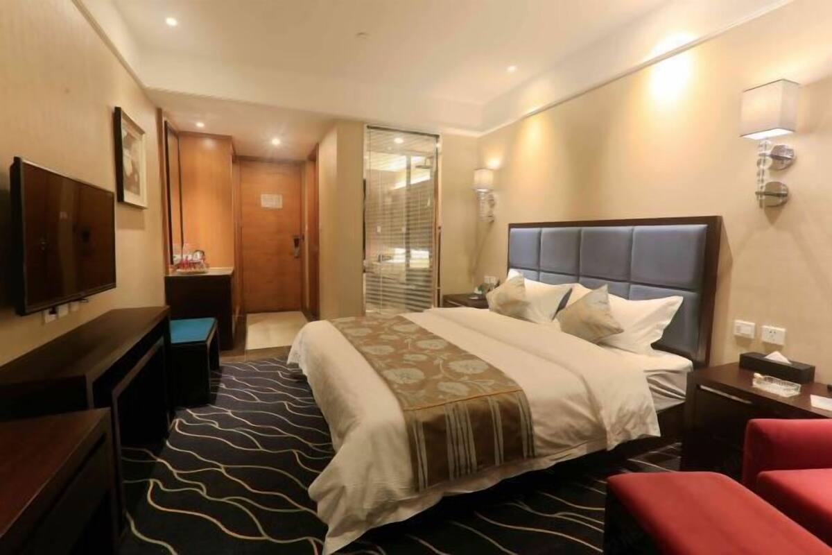 Een hotelkamer met een groot bed, een flatscreen televisie, een bureau en een rode stoel.