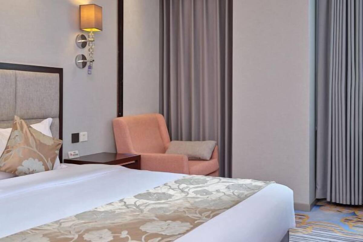Een hotelkamer met een bed, een stoel, een lamp en gordijnen.