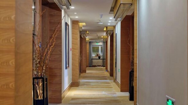 Un couloir d’hôtel avec des lambris en bois, un sol en marbre et des luminaires encastrés.
