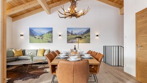 Un coin repas avec une table en bois, des chaises en cuir et un lustre. Deux appliques murales éclairent la pièce, et un tapis en peau de vache recouvre le sol.