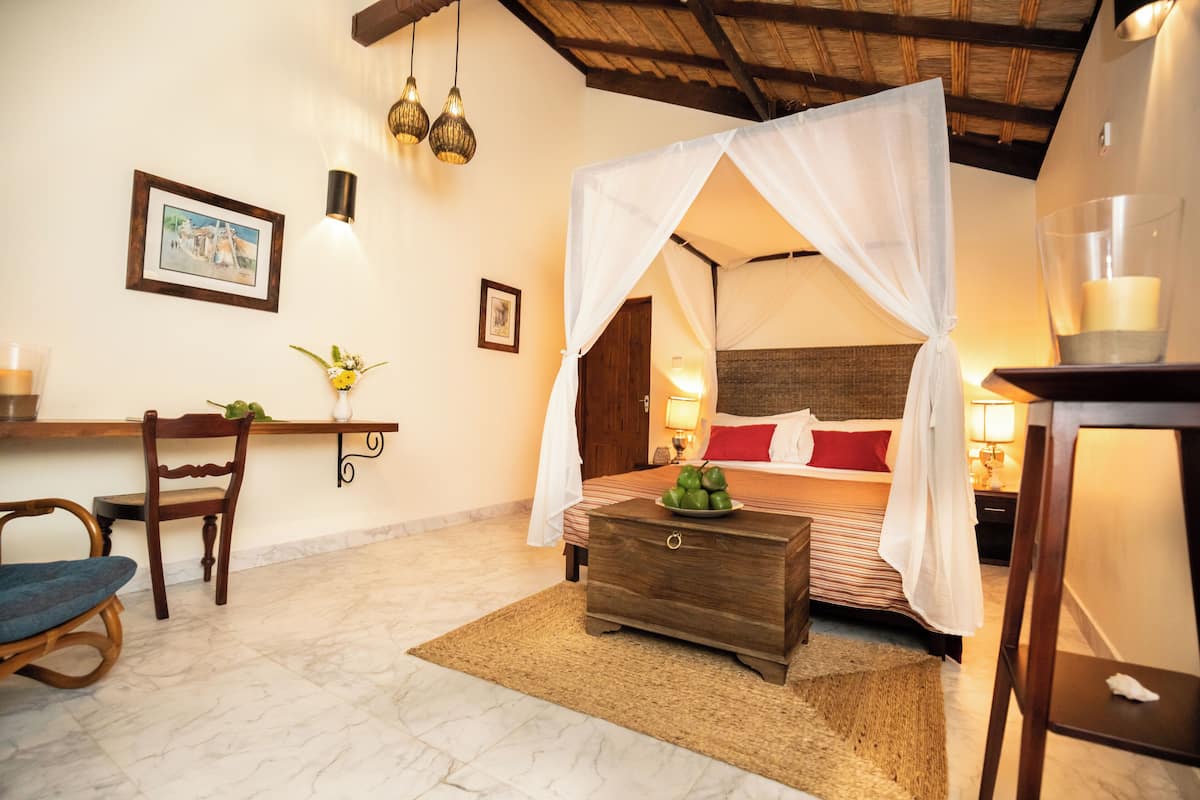 A bedroom with a four-poster bed, a wooden nightstand, a chair, and a bedside table with a lamp.