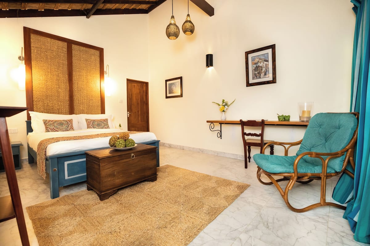 A bedroom with a bed, wooden nightstand, wicker chair, and a desk with a chair.