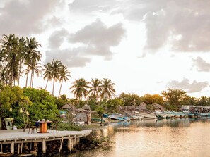 A calm waterfront with boats docked, palm trees, and traditional huts.