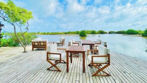 Une terrasse en bois avec des meubles d’extérieur, une étendue d’eau calme et de la verdure en arrière-plan.