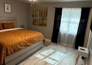 A bedroom with a bed, a nightstand, a window with curtains, and a wall with a painting.