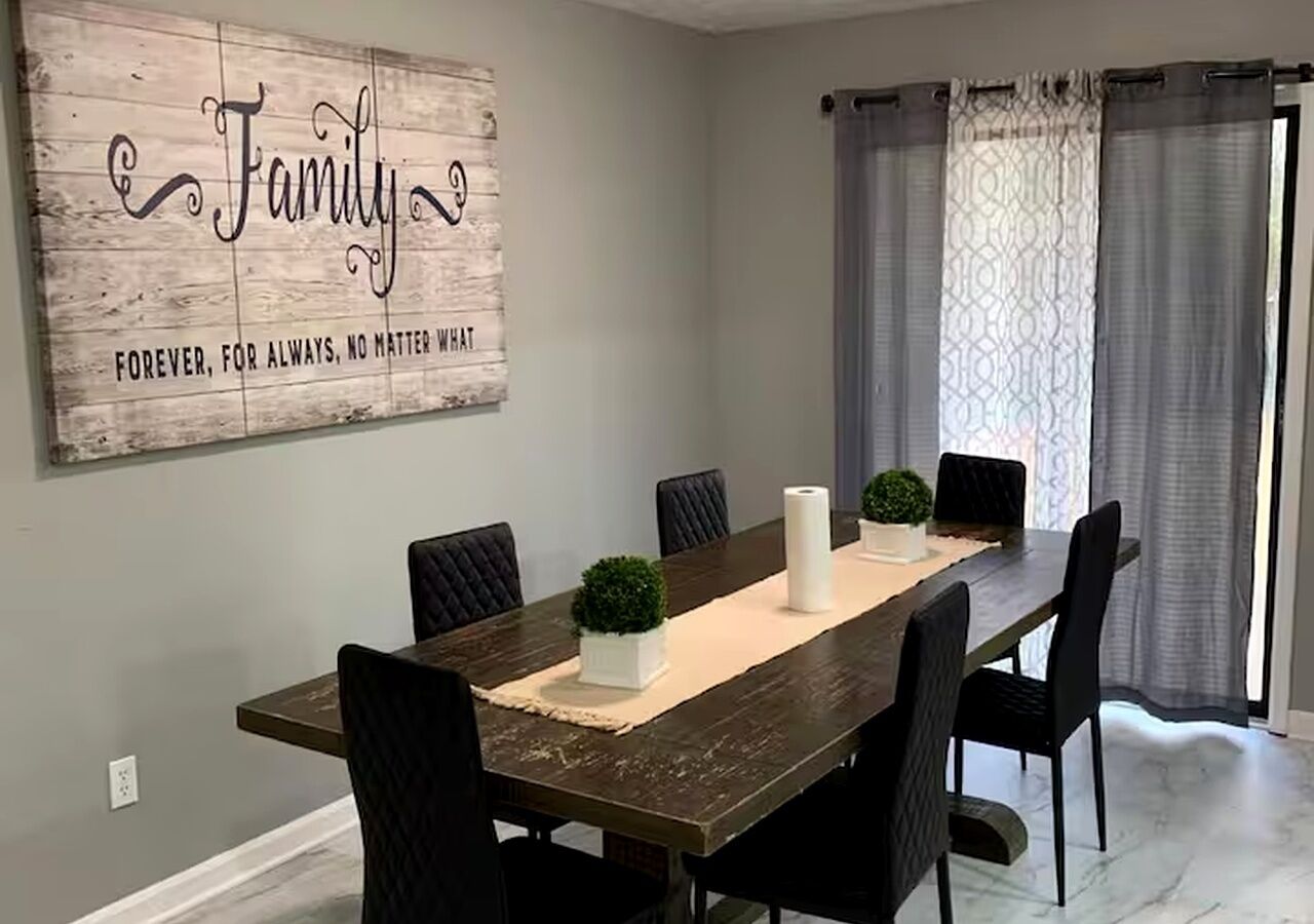 Une salle à manger avec une table en bois, des chaises noires, une plante en pot et un panneau décoratif au mur.