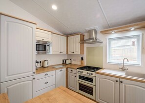 A compact kitchen with white cabinetry, a microwave, a toaster, a stove, and a sink.