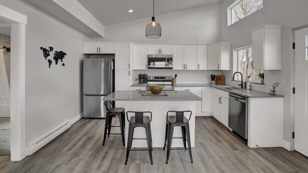 Una cocina moderna con armarios blancos, una isla central con taburetes, electrodomésticos de acero inoxidable y una lámpara colgante.