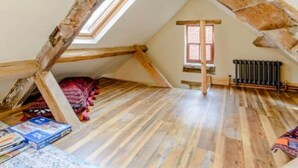 Ein Schlafzimmer im Loft-Stil mit freiliegenden Holzbalken, einer geneigten Decke und einem kleinen Fenster.