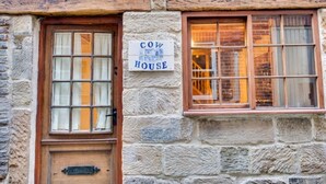 Ein Steinhaus mit einer Holztür und Fenstern, ein Schild mit der Aufschrift "COW HOUSE".